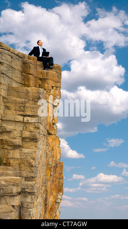 View of businessman sitting on the top of mountain and holding laptop Stock Photo