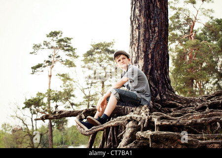 Boy sitting on roots of tree trunk Stock Photo