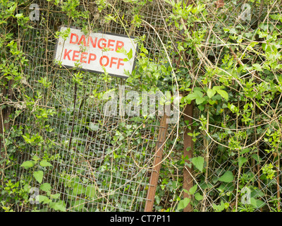 Danger keep off sign on fencing overgrown by vegetation. Stock Photo