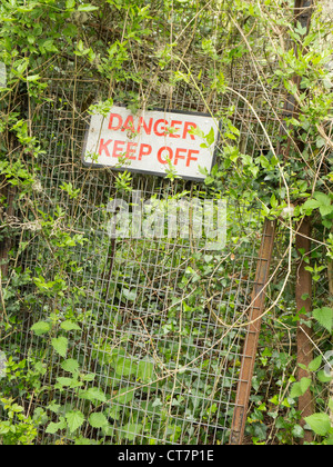 Danger keep off sign on fencing overgrown by vegetation. Stock Photo