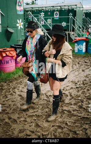 Two women in hats, sunglasses and wellies walking through the mud at the Glastonbury festival 2011 Stock Photo