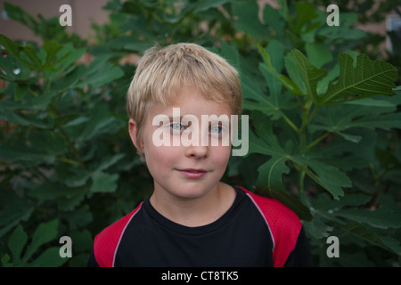 Shy ten year old boy standing in front of a fig tree and smiling at camera. Stock Photo