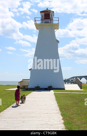 Little girl walking her Sheltie dog by a lighthouse in Prince Edward Island with the Confederation Bridge in the background Stock Photo