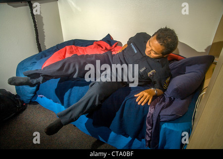 A young uniformed Asian-American firefighter jumps hurriedly from bed as he answers an alarm at a firehouse in Laguna Niguel, CA Stock Photo