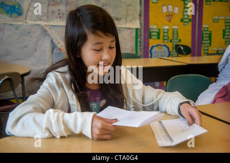 An Asian American middle school student removes a sheet of paper from an envelope in a classroom. Stock Photo