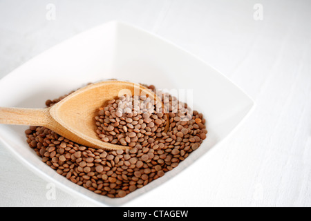 A bowl of brown lentils (Lens culinaris) with a wooden spoon Stock Photo