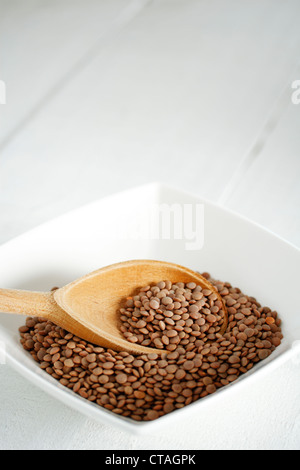 A bowl of brown lentils (Lens culinaris) with a wooden spoon Stock Photo