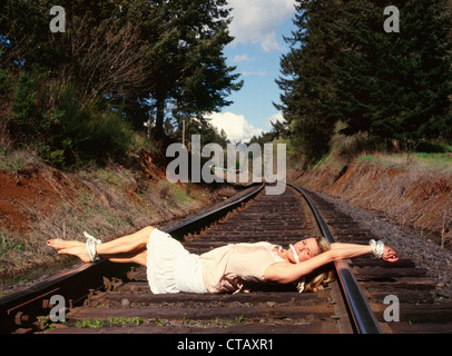 A woman tied on some railroad tracks like a 'damsel in distress.' Stock Photo