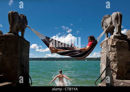 Young woman jumping into the water, man reading in hammock, Lake Starnberg, Upper Bavaria, Germany, Europe Stock Photo