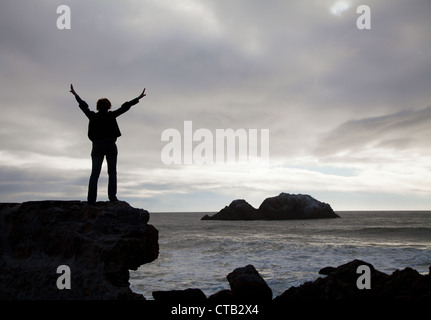 Woman staying with raised hands against sunset at the ocean Stock Photo