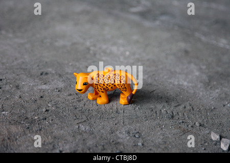 It's a photo of a toy plastic Tiger in orange color that stand on the floor on the dust. It's a kid's small toy Figurine lonely Stock Photo