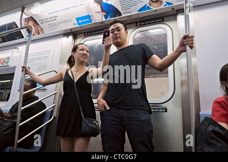 Young couple on New York City subway looking at iPhone. Stock Photo