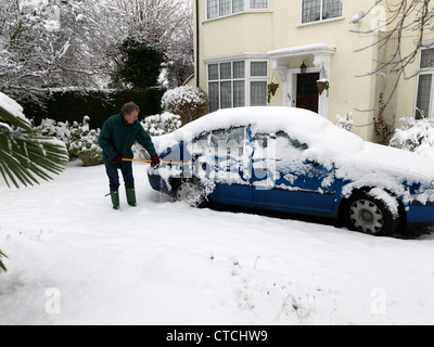 Man Using A Rubber Wonder Broom To Clear The Ice And Snow Off A Car During Winter Surrey England Stock Photo