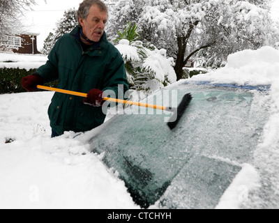 Man Using A Rubber Wonder Broom To Clear The Ice And Snow Off A Car Windscreen During Winter Surrey England Stock Photo