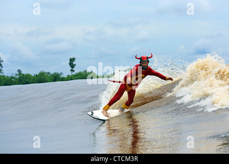 Strange man in red superhero costume river surfing a tidal bore wave on the Kampar River, also known as Bono or the 7 Ghosts. Stock Photo