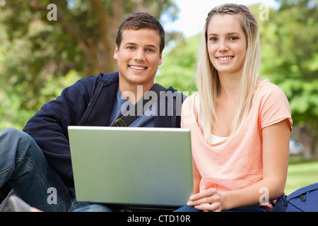 Portrait of two students laughing while sitting with a laptop Stock Photo