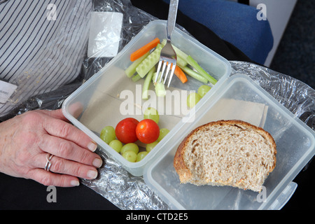 Close-up showing hand. Healthy workplace eating on budget, packed lunch on lap, salad in plastic box,  School, England, UK Stock Photo