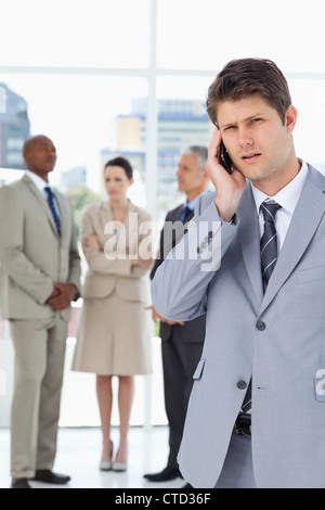 Serious businessman using a cell phone while his team is behind him Stock Photo