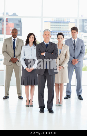Mature manager crossing his arms followed by his serious team crossing their hands Stock Photo