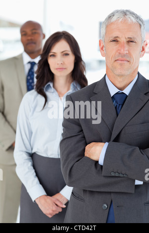 Mature manager crossing his arms seriously in front of two members of his team Stock Photo