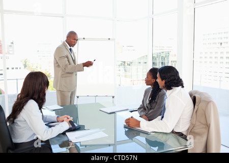 Businessman pointing to something on the flipchart to explain this to his colleagues Stock Photo