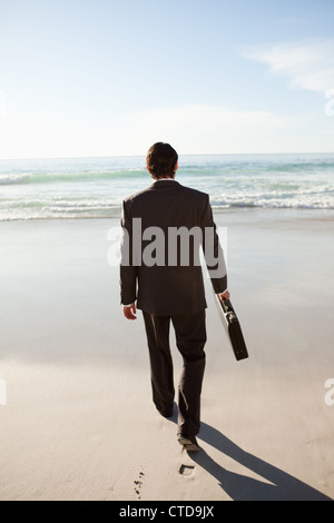 Rear view of a serious businessman walking on the beach Stock Photo