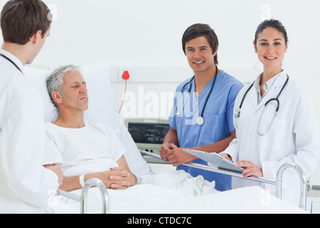 Doctor and a nurse smiling as they stand next to a patients bed Stock Photo