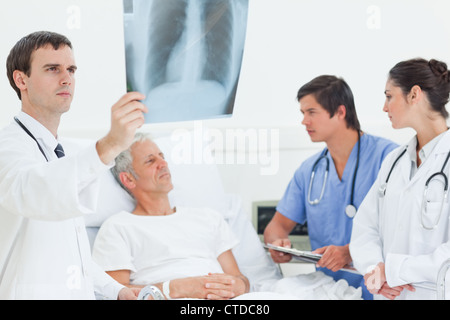 Doctor looking at an x-ray scan while standing next to a patients bed Stock Photo