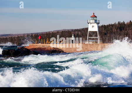 Two people on the breakwater in Grand Marais, Minnesota watch rough Lake Superior waves. Stock Photo