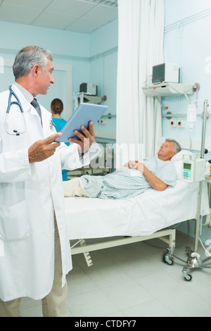 Serious doctor using a tactile tablet while looking at a patient in a bed ward Stock Photo