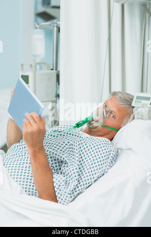 Senior male patient wearing an oxygen mask while holding a tactile tablet in his hands Stock Photo