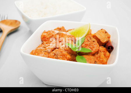 food Indian curry butter chicken in a square white bowl on a blue background, garnished with lime and thai basil. Stock Photo