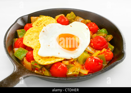 A cast iron skillet containing huevos rancheros, salsa rancheros topped with corn chips and a fried egg. Stock Photo