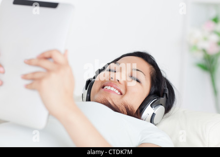 Woman lying on a couch with headphones on and a tactile tablet in her hands Stock Photo