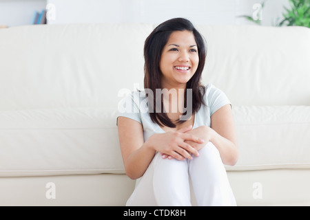 Woman smiles as she sits in front of a couch on the floor Stock Photo