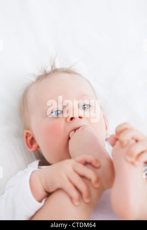 Cute baby placing her foot on her mouth Stock Photo
