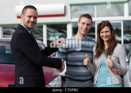 Dealer shaking hand of a man while giving him car keys Stock Photo