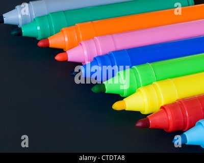 Several colored felt pens with caps off isolated on black background. Stock Photo