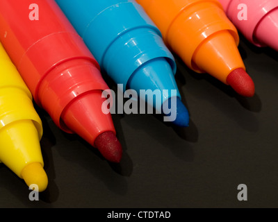 Several colored felt pens with caps off isolated on black background. Stock Photo