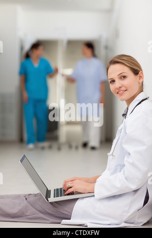 Woman doctor sitting on the floor while typing on a laptop Stock Photo