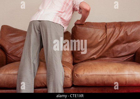Man searching behind sofa cushions for lost items. Stock Photo