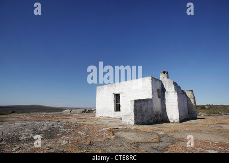 An old dilapidated structure which was once lived in now stands alone and empty against a deep blue sky