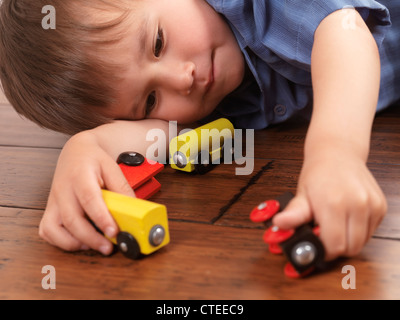 Two year old boy playing with a colorful wooden toy train on hardwood floor Stock Photo