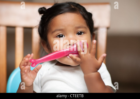 hispanic baby girl learning to hold a spoon by herself Stock Photo