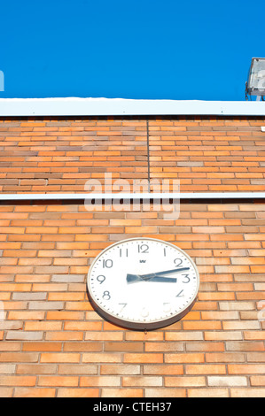 White clock on a orange, brick wall with the time reading a quarter past three in the afternoon Stock Photo