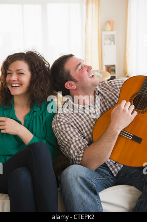 USA, New Jersey, Jersey City, Couple sitting on sofa, man playing guitar Stock Photo