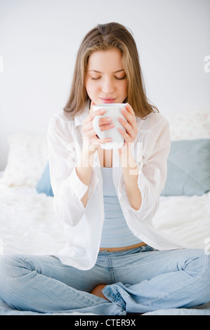 USA, New Jersey, Jersey City, Woman sitting on bed drinking coffee Stock Photo