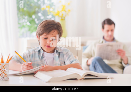 USA, New Jersey, Jersey City, Boy (10-11 years) doing homework at table with father sitting in background Stock Photo