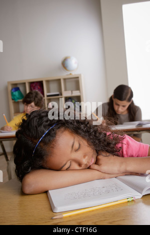 USA, California, Los Angeles, girl (10-11) napping on desk with girl (12-13) and boy (10-11) in background Stock Photo
