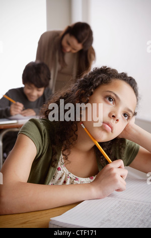 USA, California, Los Angeles, schoolgirl (10-11) holding pencil with boy (12-13) and teacher in background Stock Photo